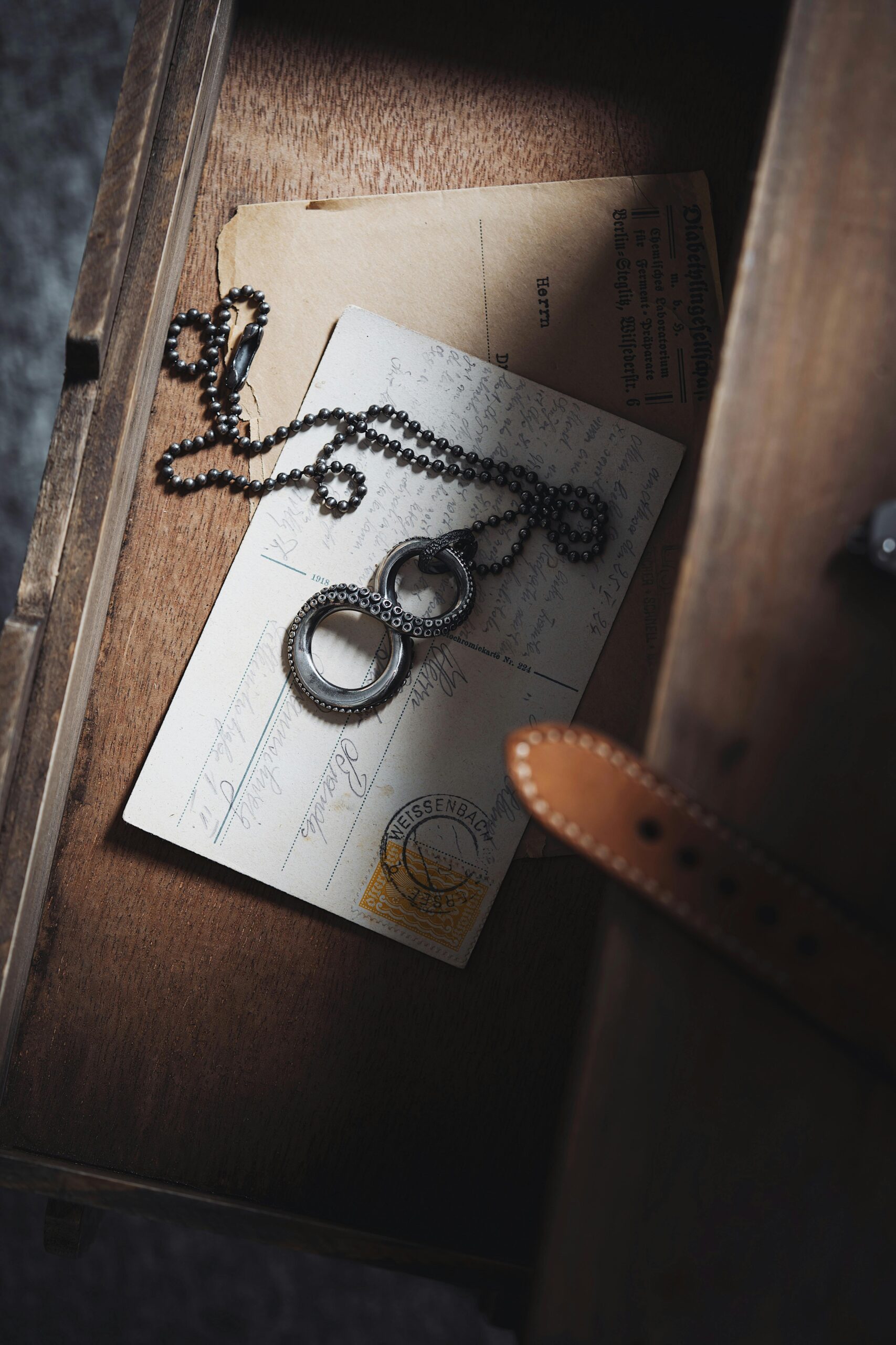 A vintage chain necklace placed atop aged postcards in a wooden drawer, evoking nostalgia.